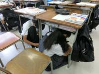 避難訓練で机の下に潜ってる画像